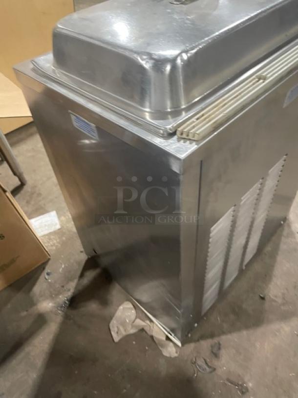 Commercial stainless steel ice cream freezer, top lid, ventilation slats, used condition, visible scratches, industrial use.