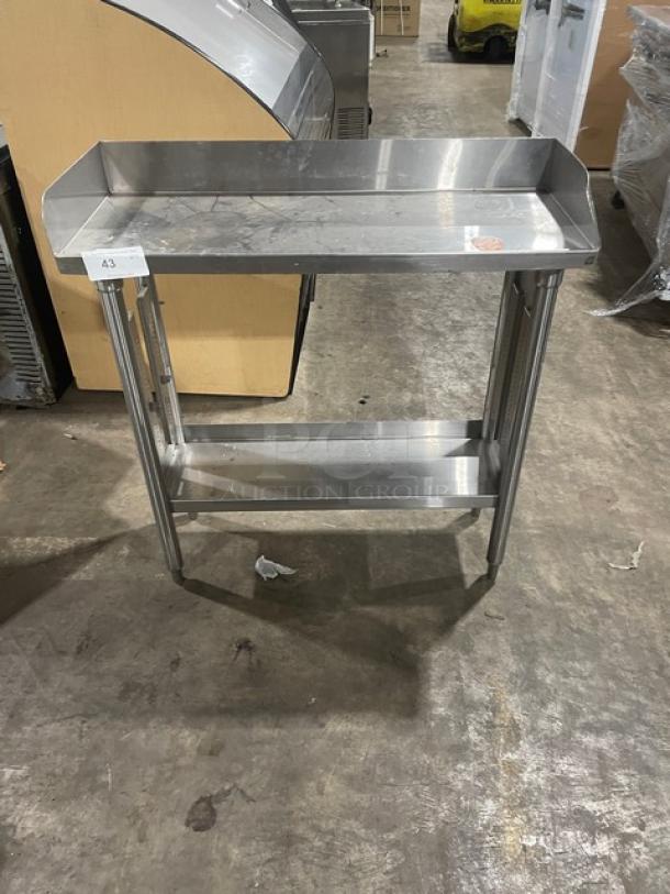 Stainless steel utility table with raised edges and lower shelf. Used condition with a visible sticker. Auction tag number 43.