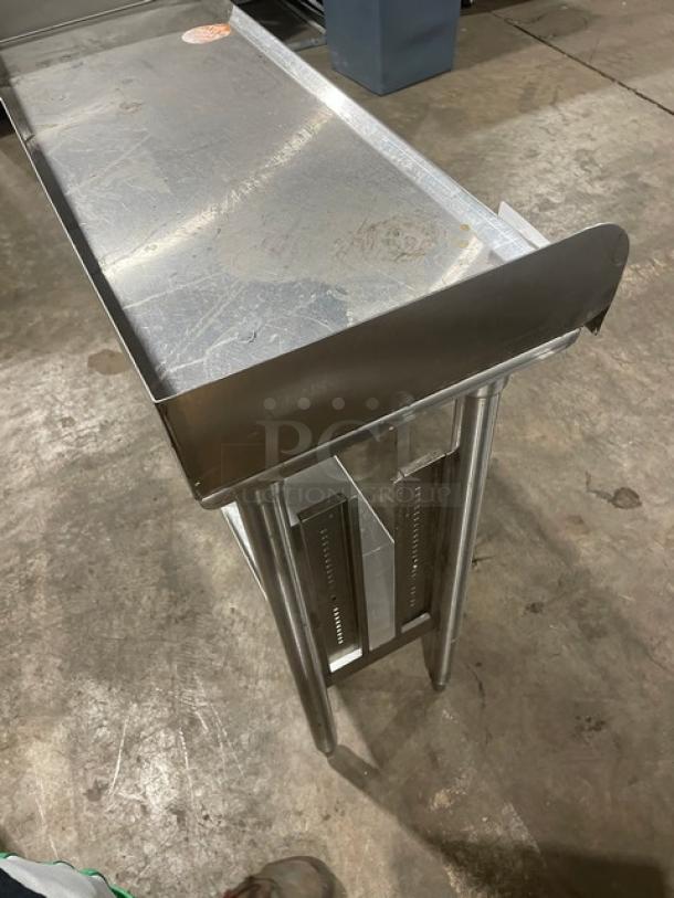 Stainless steel commercial prep table with raised edges, sturdy legs, and visible surface markings, in used condition.