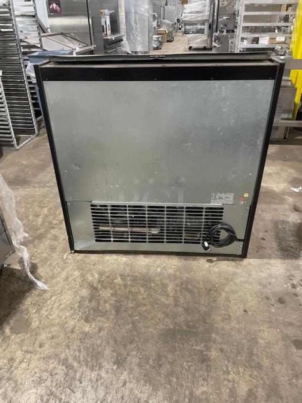 Commercial refrigeration unit, stainless steel, black frame, vented back, visible power cord, used condition.