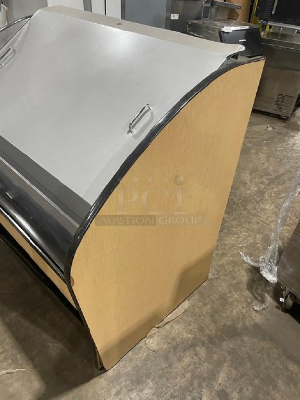 Commercial refrigerated display case with a curved top, wooden side panels, and metal accents, in good condition.