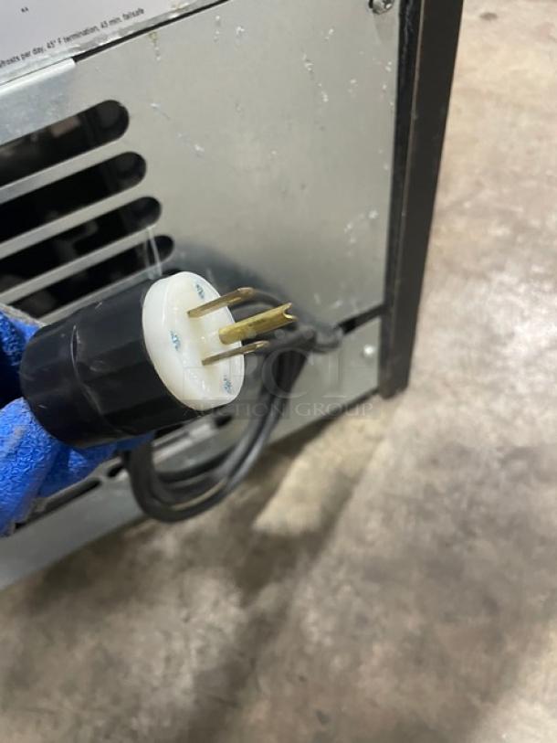 Industrial power plug with blue handle attached to a metal equipment body. Plug features three prongs in good condition.