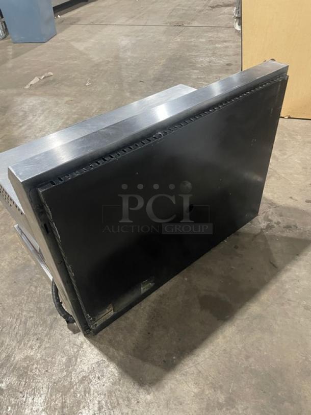 Black and silver commercial oven door with visible wear, showing a vented top edge. No labels or markings visible.