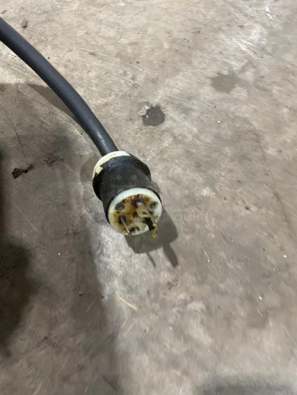 Power cable with a worn, industrial-grade plug. Visible corrosion on prongs. Black cable suggesting heavy-duty use.