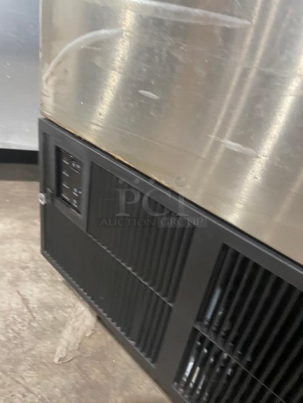 Stainless steel commercial refrigerator with black vent panel, showing wear and scratches on surface.