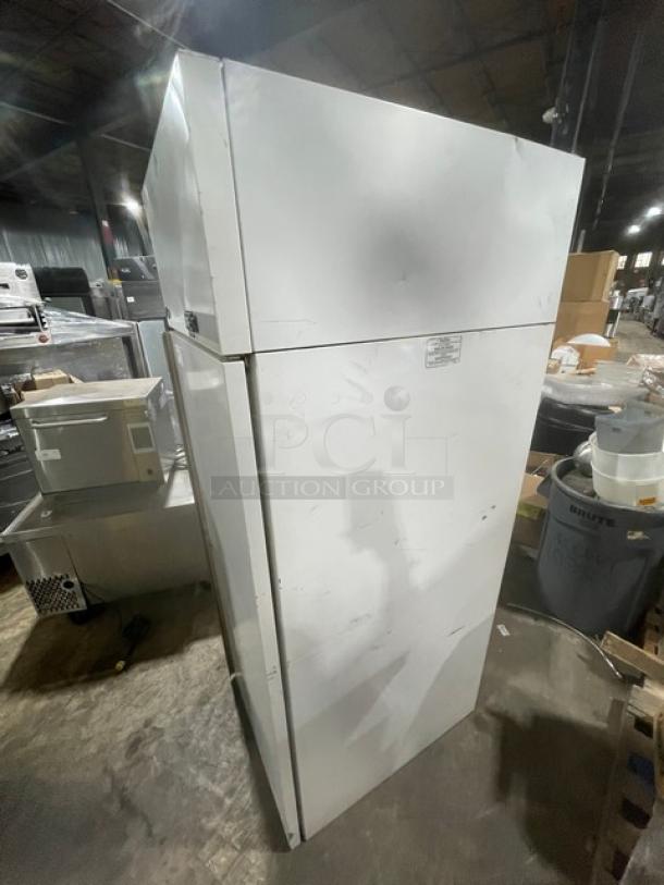 Commercial double-door stainless steel refrigerator, slight dents, and scratches, label denotes model and energy rating.