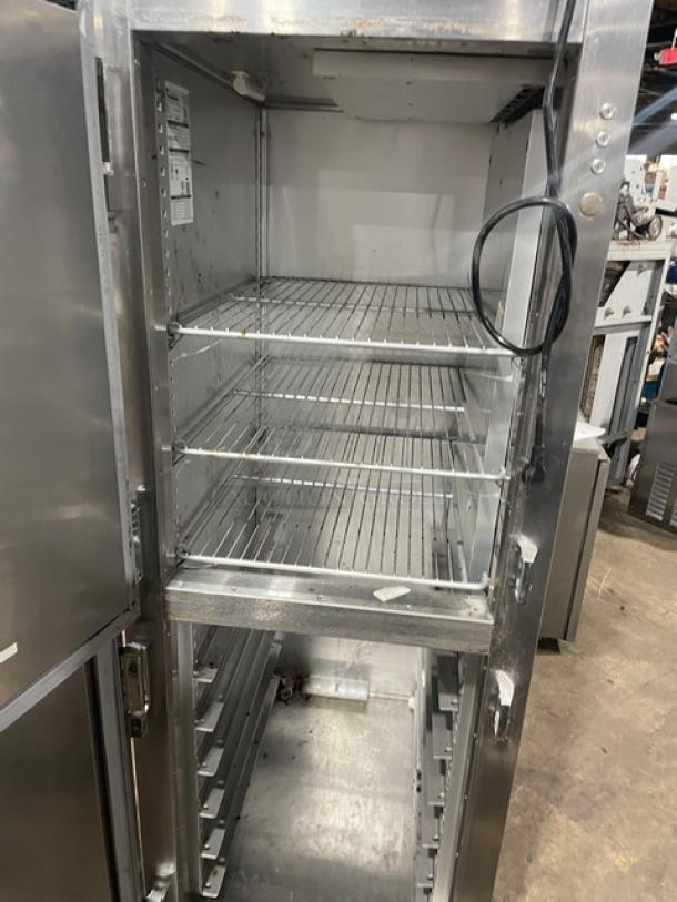 Commercial stainless steel warming cabinet with multiple wire shelves, open door, visible electrical cord, and interior labels.