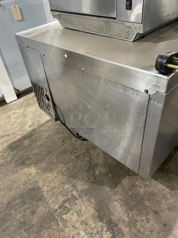 Commercial stainless steel refrigeration unit with visible surface wear and ventilation panel on the side.