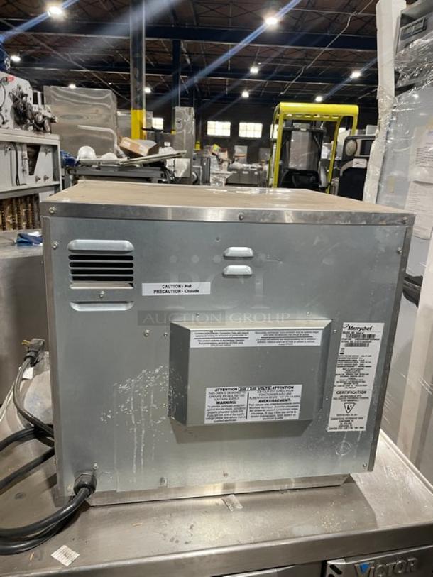 Commercial metal ice maker in a warehouse setting, featuring caution and specification labels; overall good condition.