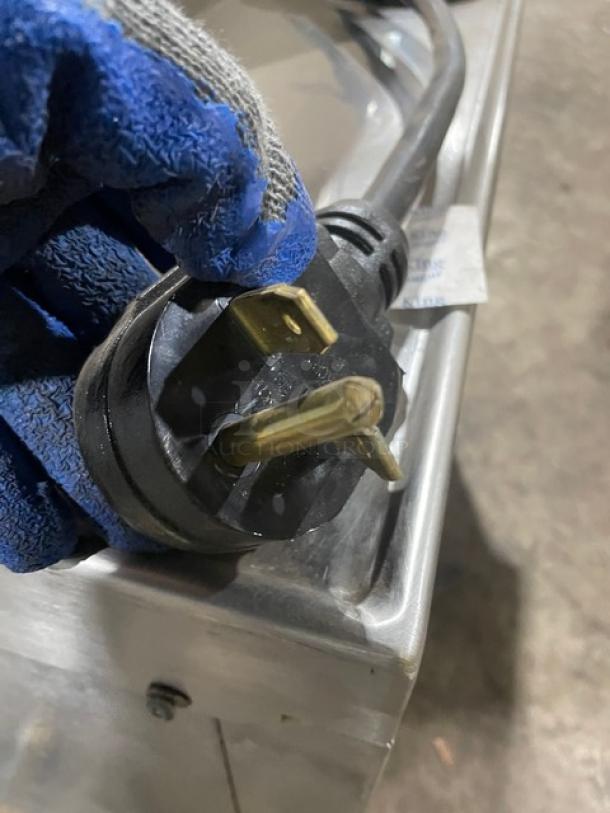 Heavy-duty electrical plug, three-prong, black with gold contacts, slight wear, blue-gloved hand holding, metal surface background.