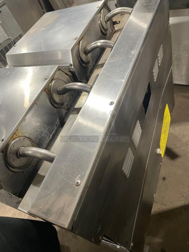 Industrial stainless steel heat exchanger, three coil entries, visible wear, yellow safety label, used condition.