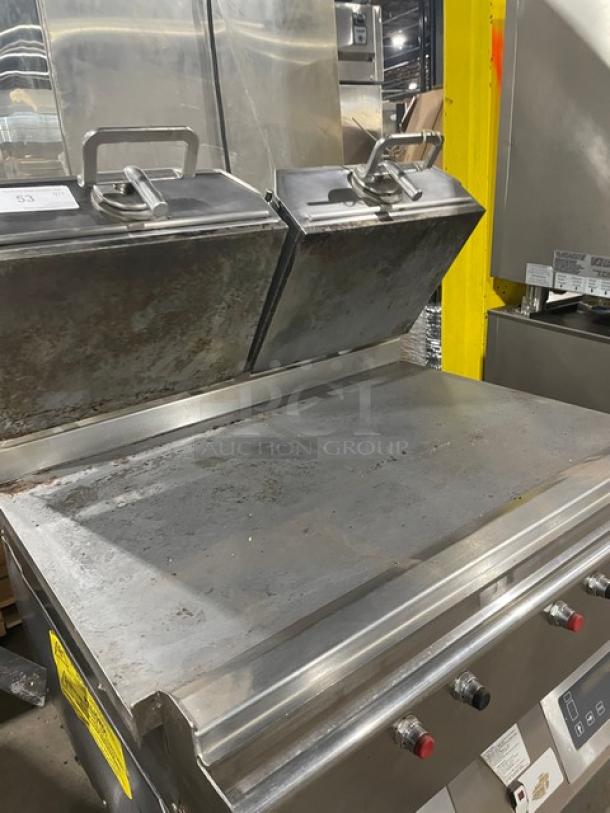 Commercial stainless steel grill with dual hoods, showing signs of use. Control knobs and label indicating settings visible.