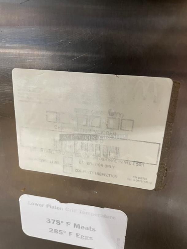 Stainless steel commercial grill with inspection label showing certification number and operating temperatures for meats and eggs.