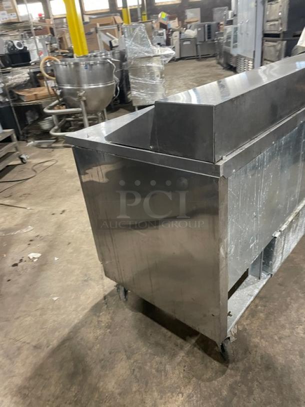Stainless steel commercial kitchen counter on wheels. Slightly worn condition. Suitable for high-traffic culinary use.
