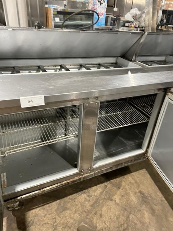 Commercial stainless steel refrigerated prep table with glass doors, wire shelving, and condiment slots. Visible label: "54".