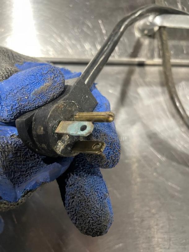 Electrical plug with wear, held in gloved hand. Visible corrosion on prongs, indicating need for repair or replacement.
