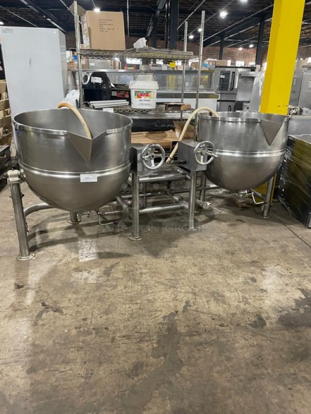 Two large industrial stainless steel steam kettles with control valves, in good condition, on warehouse floor.