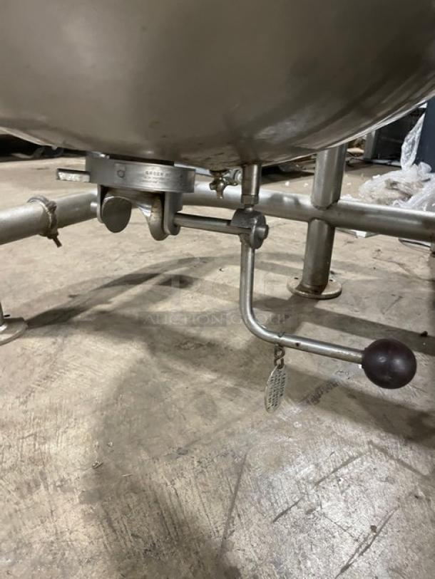 Stainless steel industrial mixer with tilt mechanism, mounted on metal legs. Appears in good condition, floor standing model.