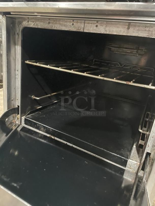 Industrial oven with open door, showing metal rack and interior. Used condition, with visible wear and stainless steel exterior.