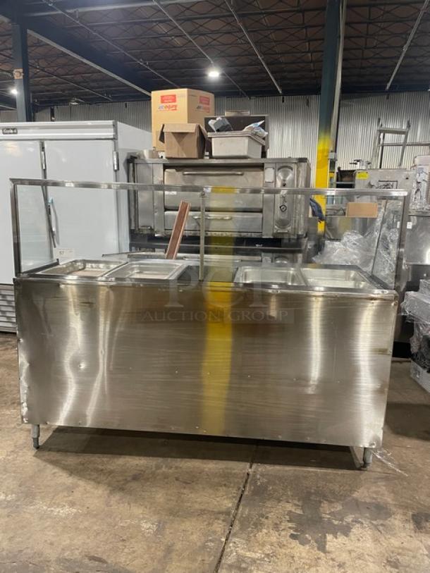 Stainless steel commercial food serving counter with glass sneeze guard, showing three compartments, in good used condition.