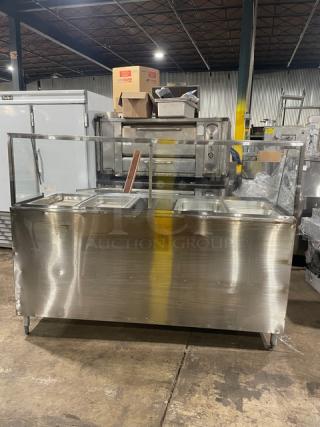 Stainless steel commercial food serving counter with glass sneeze guard, showing three compartments, in good used condition.