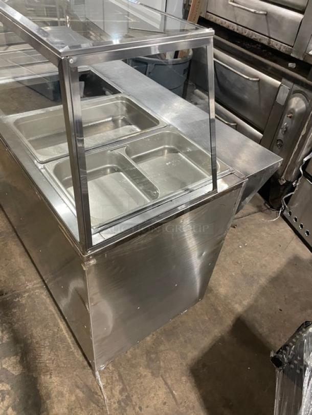 Stainless steel food service counter with glass sneeze guard and multiple compartments, in good condition.