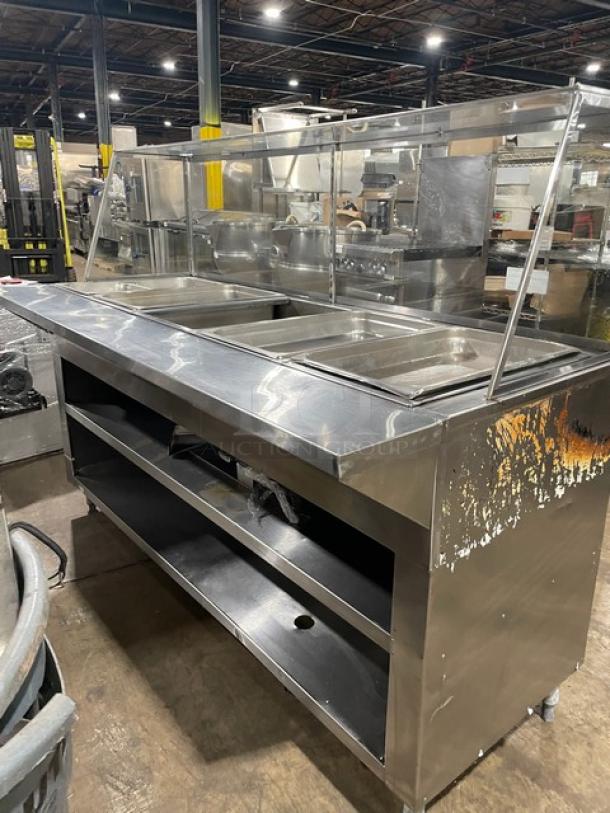 Stainless steel buffet serving station with three compartments, glass sneeze guard, some surface rust on the right side panel.