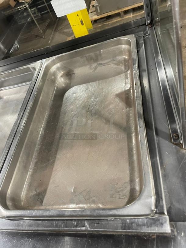 Stainless steel food warming tray, used, rectangular, industrial kitchen setting, visible wear and scratches.