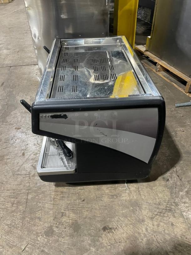 Commercial espresso machine, stainless steel and black, dual steam wands, used condition, no visible brand markings.