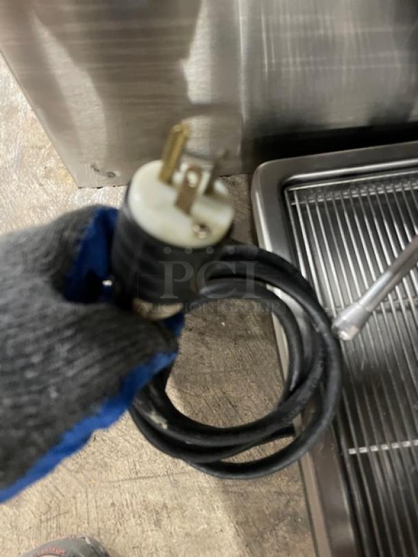 Power cord with three-prong plug, black insulation, in good condition. Coiled near industrial stainless steel equipment.