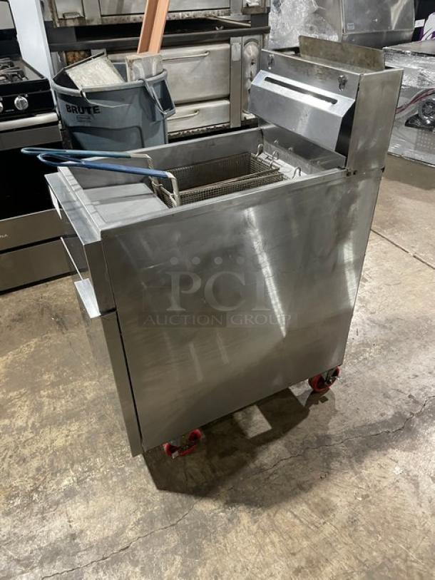 Commercial steel deep fryer on wheels with dual baskets, industrial setting, minor wear, suitable for restaurant use.
