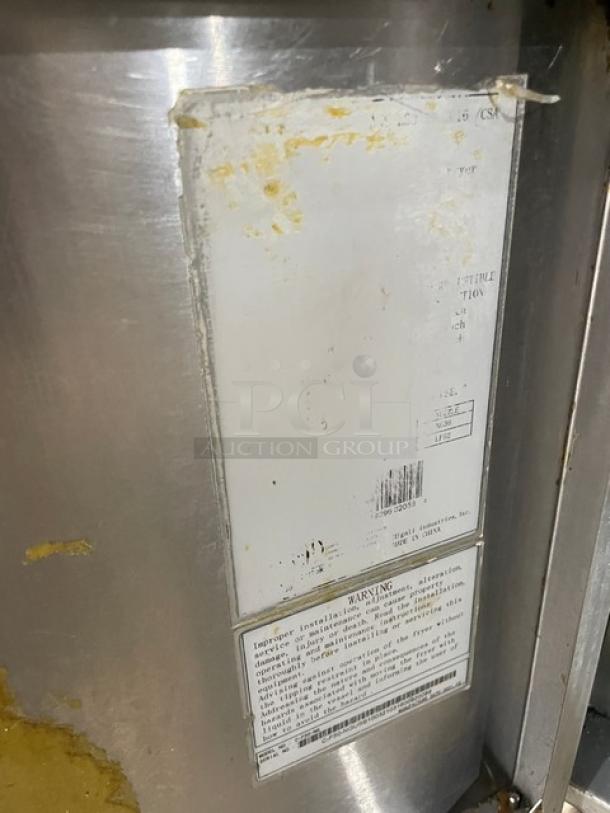 Commercial stainless steel appliance with visible wear, featuring a barcode and warning label detailing installation instructions.