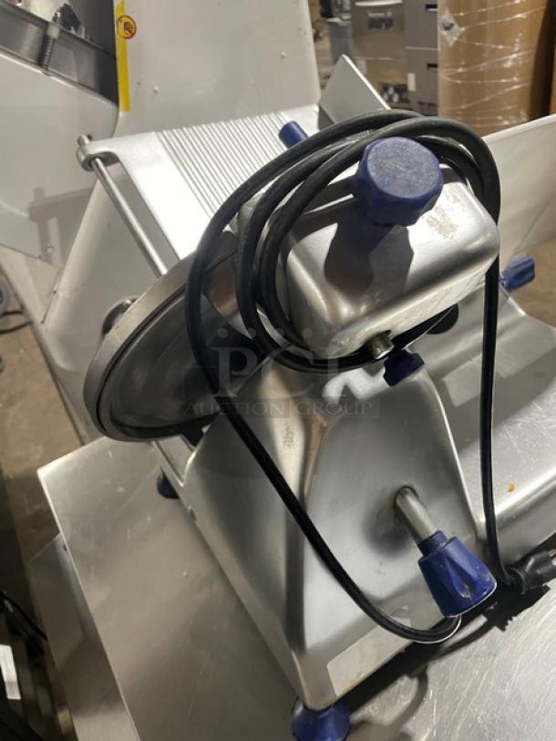Commercial meat slicer with blue knobs, metal body, and coiled power cord in good condition.