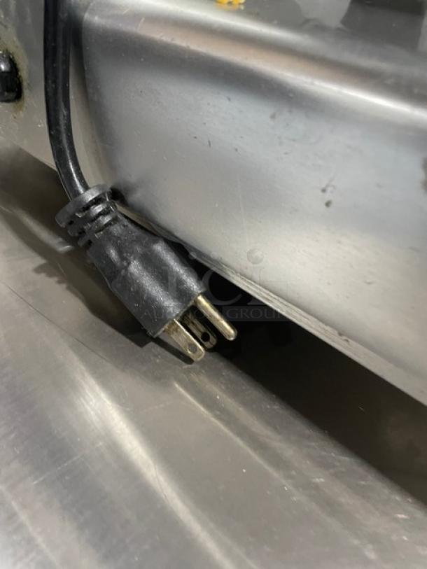 Power cord with three-prong plug attached to stainless steel equipment, showing wear. Suitable for heavy-duty appliances.