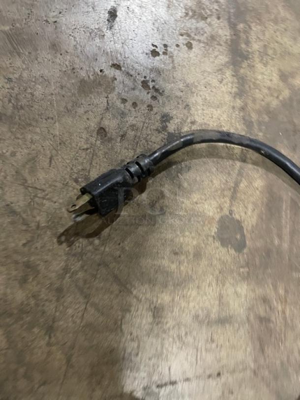 Black electrical power cord with three-prong plug, slightly worn, on a concrete surface with visible scratches and stains.