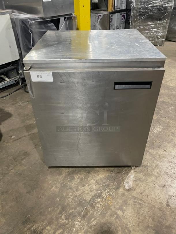 Stainless steel commercial refrigerator, square shape, front handle, moderate wear. Auction tag 65 visible on the front.