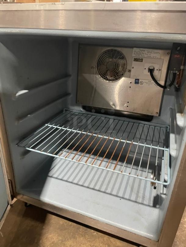 Commercial refrigerator interior, stainless steel finish, wire shelf, cooling fan, and wiring visible; model info not shown.