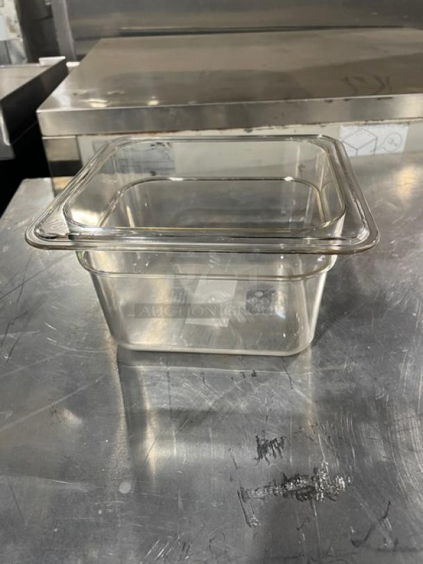 Clear polycarbonate food storage container, square, excellent condition, with measurement markings on side, sits on metal surface.