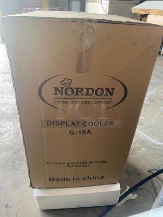 Nordon G10A countertop merchandiser display cooler in box. Features black single glass door, poly coated wire racks, lock, and keys.