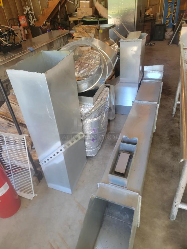 Collection of metal HVAC ductwork components in a garage, including vents and fittings in used condition.