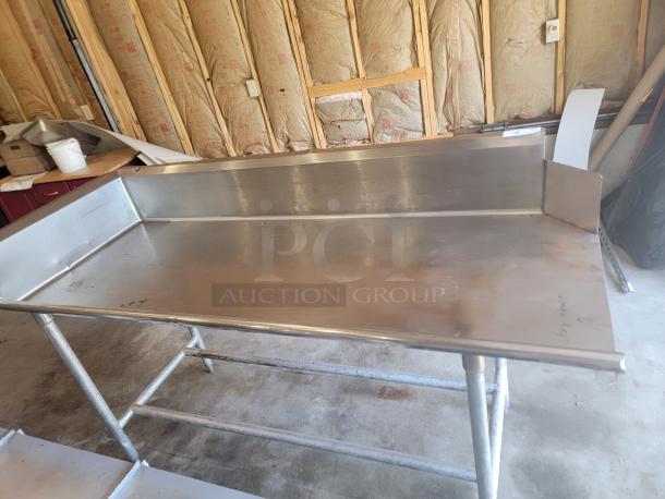 Stainless steel work table with raised edges, sturdy metal legs, minor wear. Ideal for commercial kitchens or workshops.