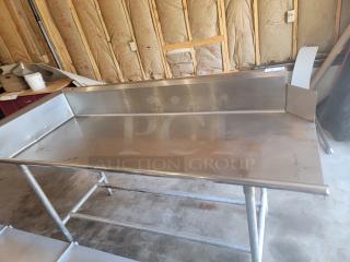 Stainless steel work table with raised edges, sturdy metal legs, minor wear. Ideal for commercial kitchens or workshops.