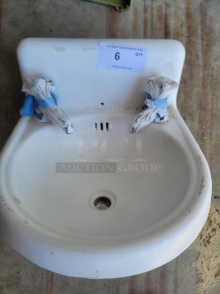 White ceramic wall-mounted sink with taped faucets, signs of wear, and auction label number 6 from PCI auctions.