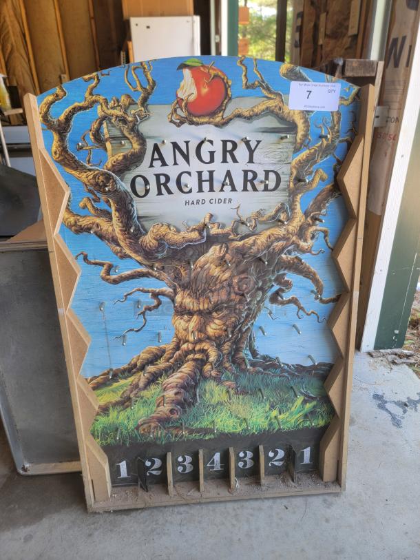 Angry Orchard promotional sign featuring a twisted tree design, numbered slots at the bottom, and a label marked "7 QTY."
