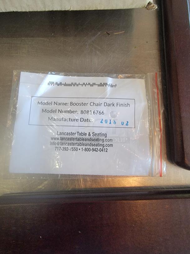 Lancaster booster chair dark finish, model 80816766, manufactured 2018, labeled with contact info, in packaging.