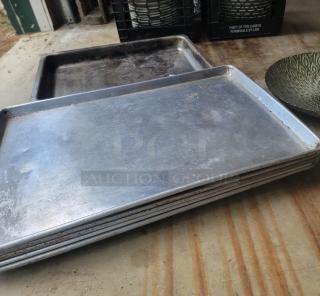 Stack of vintage metal baking trays, well-worn with visible signs of use, resting on a wooden surface.