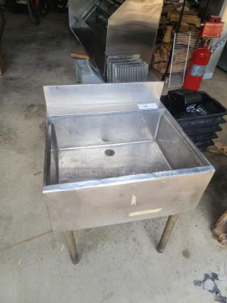 Stainless steel utility sink with backsplash, worn condition, visible drain hole, on four metal legs, auction tag #12.