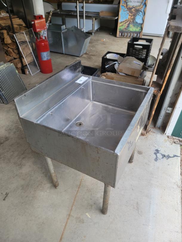 Stainless steel utility sink with high back and drain, standing on four legs, in used condition. Auction tag labeled "32".