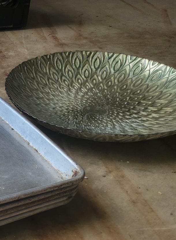 Ornate metal dish with intricate peacock feather pattern, antique finish, excellent condition, beside stacked metal trays.