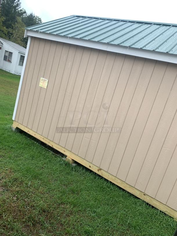 Tan storage shed with metal roof on grassy lawn, wooden base. Good condition. Label affixed to side indicates specifications.